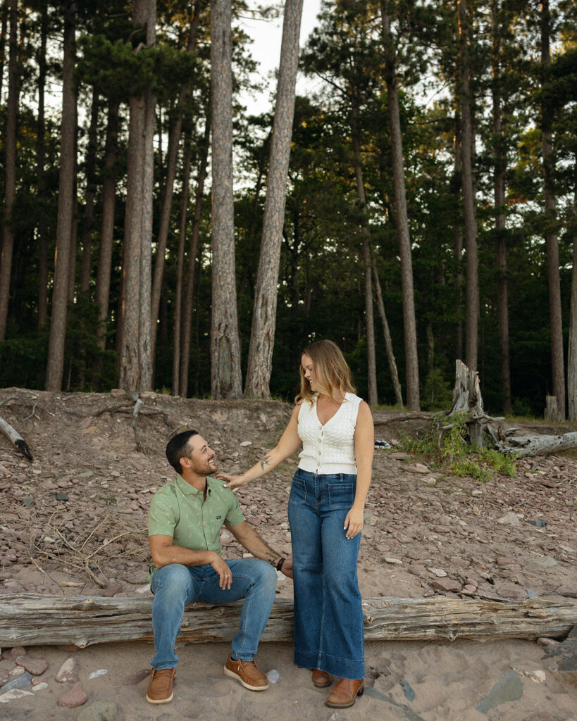 Couple standing among tall pine trees and rocks during their Little Presque Isle engagement photos.