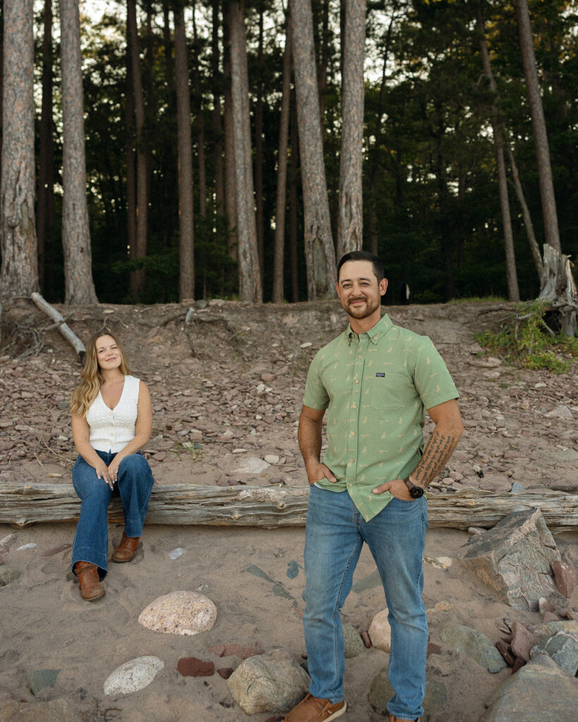 Couple posing among tall pine trees and rocks during their Little Presque Isle engagement photos.