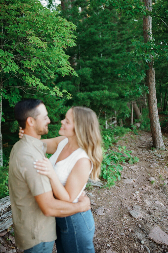 Soft-focus film photo of a couple embracing along a wooded trail at Little Presque Isle.