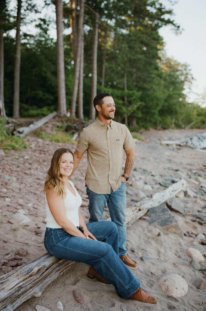 Couple posing beside driftwood along the rocky shoreline at Little Presque Isle.